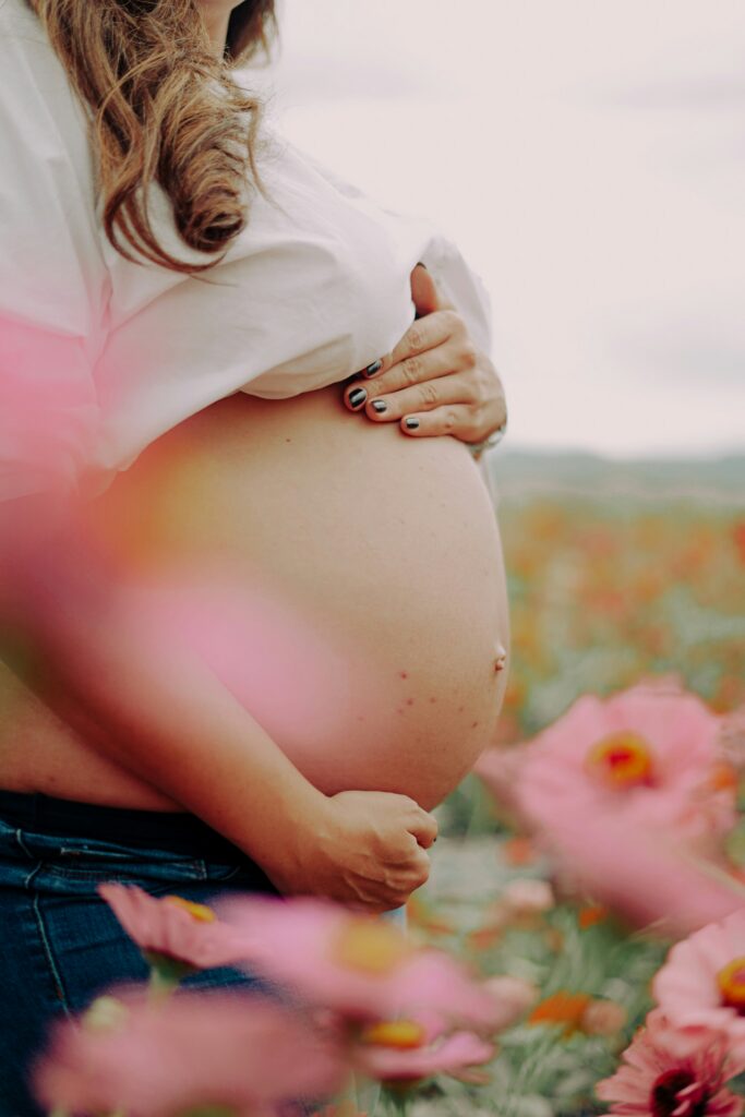 Close crop of a pregnant belly in a flower field, hand resting on top, soft golden light.