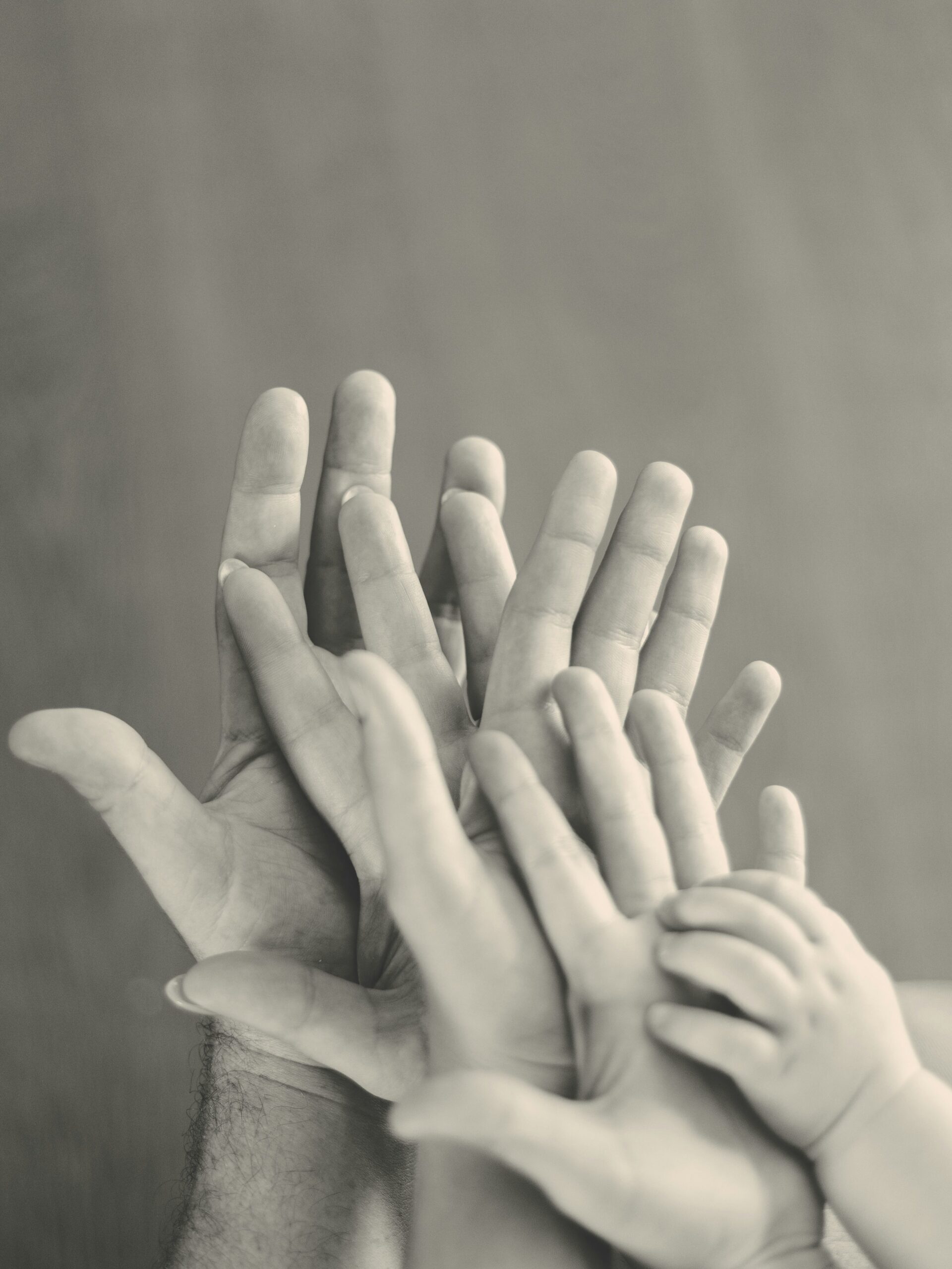 Black and white photo of four generations of hands stacked on top of each other, from an adult down to a baby.