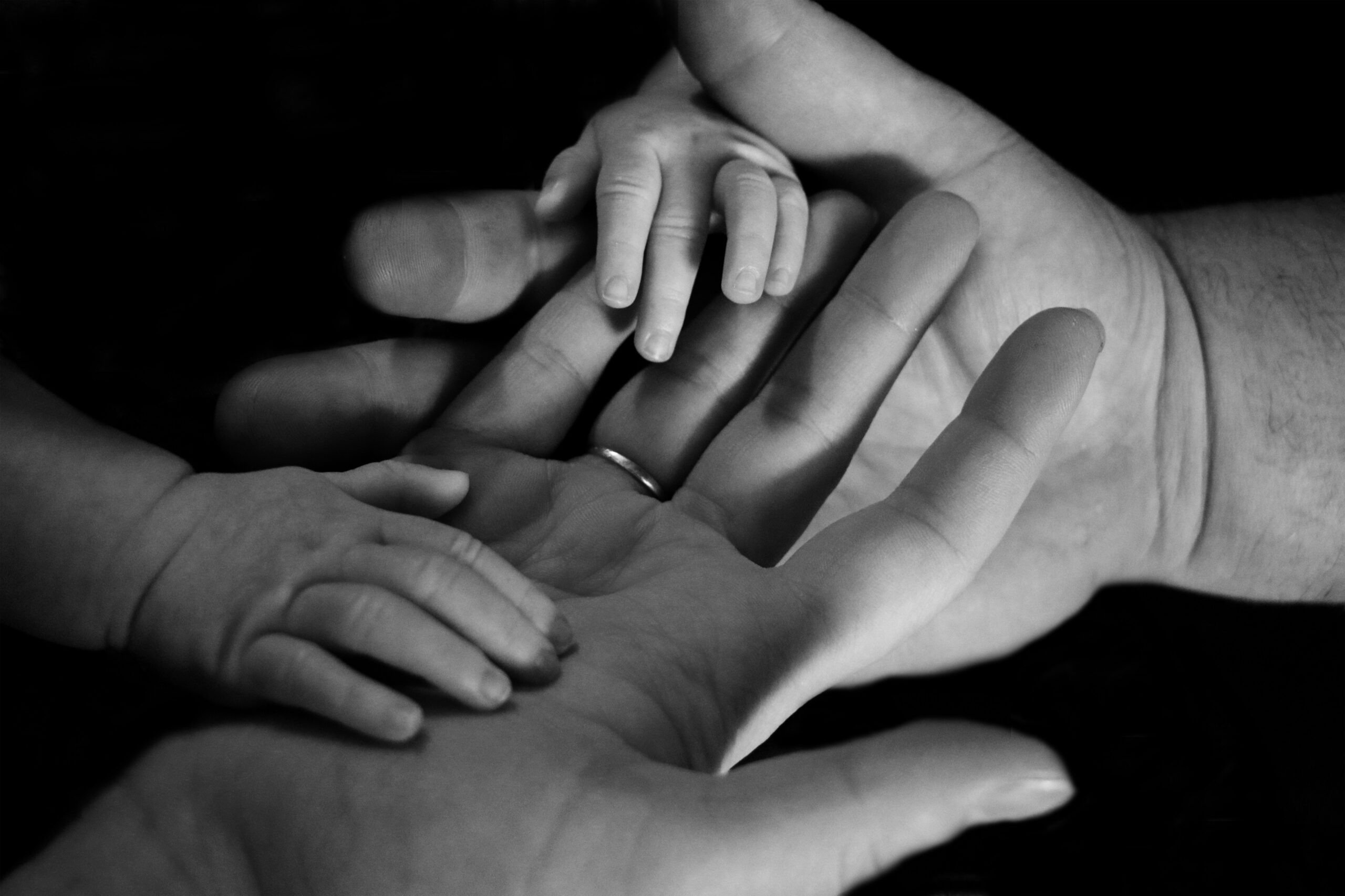 Black and white close-up of a parent's and child's hands stacked together, a baby's hand resting on top.