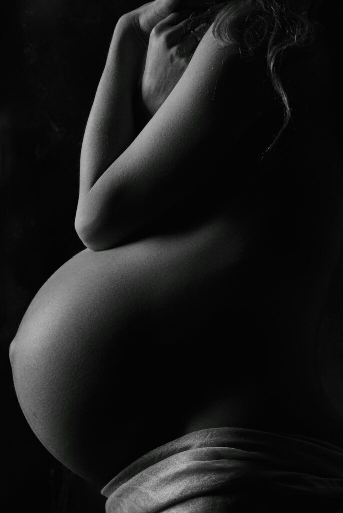 Artistic black and white maternity portrait, close crop of a pregnant belly and crossed arms, soft studio lighting.