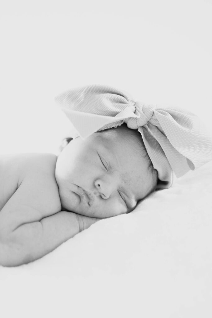 Black and white close-up of a sleeping newborn wearing a large fabric bow headband.