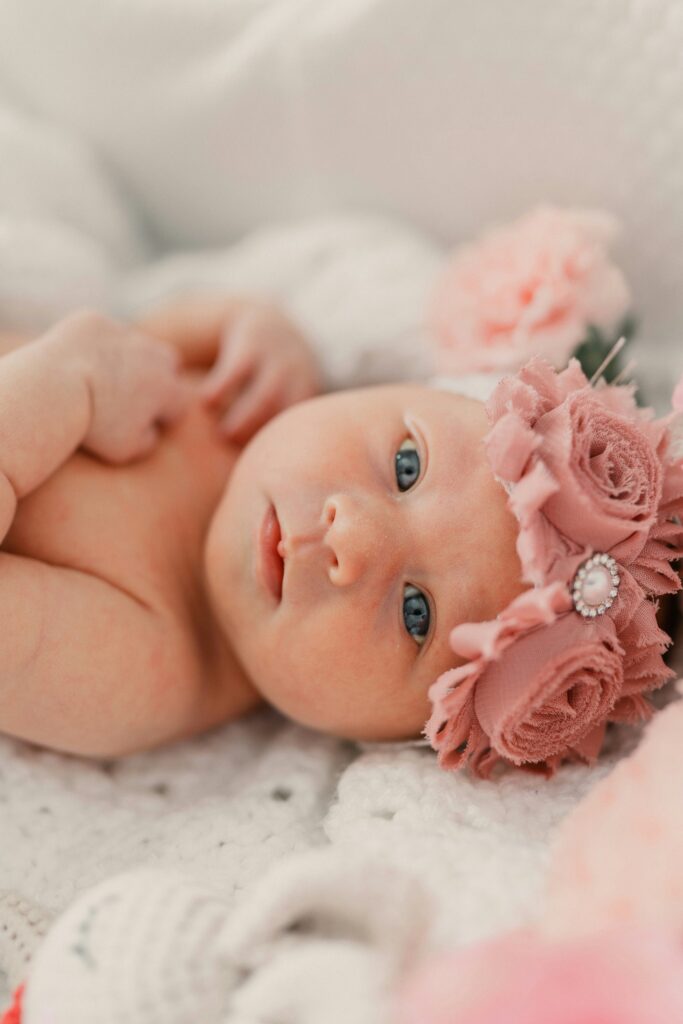 Close-up of an alert newborn baby with blue eyes, wearing a dusty rose floral headband.